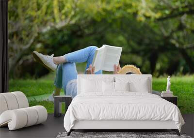 Happy woman lying on green grass reading a book in the park (outdoors) Wall mural