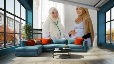 Pregnant muslim woman with her muslim female doctor in clinic, Gynecology consultation Wall mural