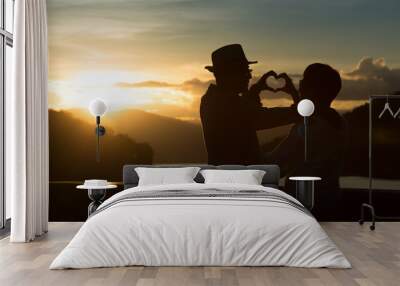 Silhouette of image of happy romantic senior couple making heart shape with hands outdoor at sunset  background Wall mural