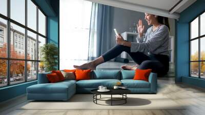 Sporty young Asian woman exercising at home, watching fitness video on Internet or having online fitness class, using smartphone, living room interior, copy space Wall mural