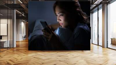 Young woman using a smartphone in her bed at night Wall mural