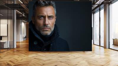 A close-up portrait of a handsome man with gray hair and blue eyes, wearing a stylish black coat. The background is dark, emphasizing his facial features and serious expression. Wall mural