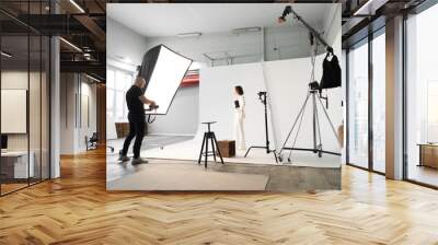 Fashion photography in a photo studio. Professional male photographer taking pictures of beautiful woman model on camera, backstage Wall mural