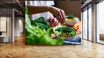 female hand pours green onions in a bowl with green peas, cucumbers, carrots, lettuce and dill stand Wall mural