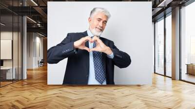 Mature businessman making heart shape with hands, smiling, on grey background. Wall mural