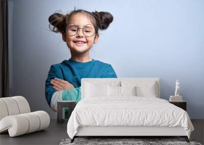 Portrait of cute swarthy caucasian little girl with glasses, arms crossed and funny hairstyle, beautiful happy child smiling and laughing looking at camera isolated in studio Wall mural