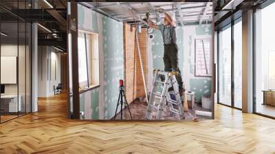 Room repair. Interior finish. young builder makes a plasterboard ceiling, standing on a stepladder Wall mural