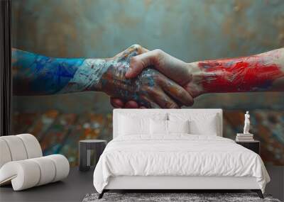 Two hands shaking, one painted with blue and white colors, the other with red. The background is textured and blurred, with a wooden floor covered in colorful paint splatters. Wall mural