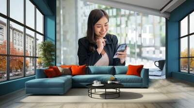 Asian business woman lightly smile when it's time to take a break with a smartphone at the office. Wall mural