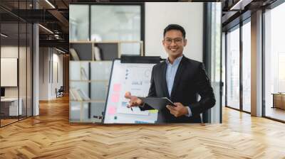 Asian businessman in a suit is standing in front of a white board with a presentation. Wall mural