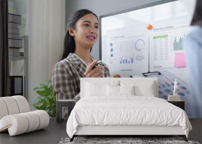 Asian businesswoman confidently explains charts to colleague in modern office meeting, embodying teamwork and communication Wall mural