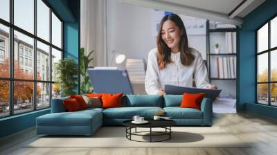 Asian businesswoman is smiling while working from her home office and using a tablet computer for a video conference call Wall mural