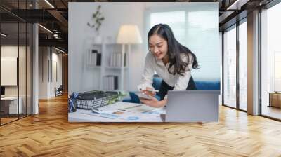 Asian businesswoman is standing at her desk and using a smartphone, working on a new project Wall mural