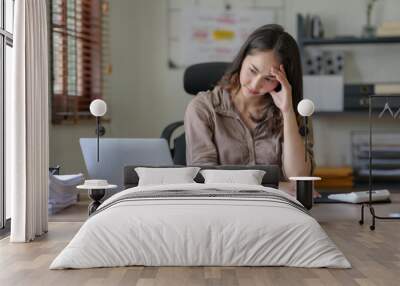 Asian businesswoman sitting in the office feeling tired, stressed or exhausted from a long day at work. Wall mural