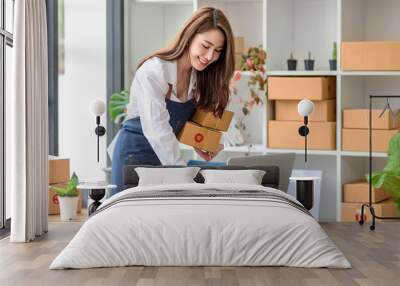 Beautiful young Asian business owner woman prepare parcel box and check online orders of product for deliver to customer. Shopping Online concept. Wall mural