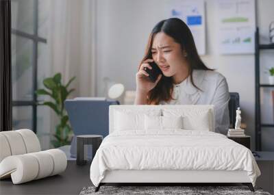 Businesswoman is having a stressful working day at the office while talking on the phone and looking at her tablet Wall mural