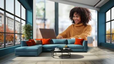 Cheerful young african american woman using computer laptop in coffee shop. Wall mural