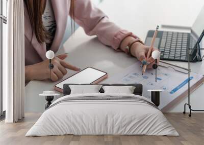 Close-up of a businesswoman hand holding a pencil with documents and using smartphone a blank white screen at the office. Mock up. Wall mural