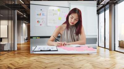 Focused businesswoman analyzing financial data on laptop in modern office, surrounded by papers and sticky notes, exuding ambition and determination Wall mural