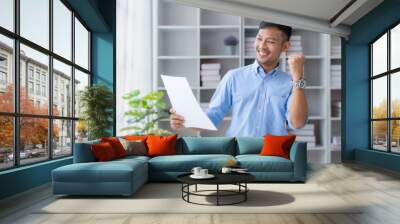 Happy asian businessman raising hands with victory smiling happily with document and laptop computer. The concept of success at work. Wall mural