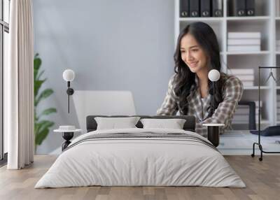 Happy smiling Asian businesswoman using laptop computer in the office. Beautiful young Asian female shopping or chatting online in social networks, freelance working on laptop projects. Wall mural