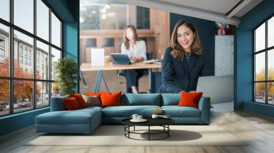 Portrait of young asian businesswoman sitting at her office looking at camera. Wall mural