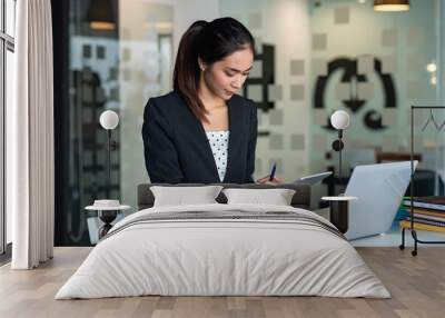 Side view of young Asian businesswoman holding a tablet sitting at the office. Wall mural