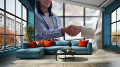 Two business professionals shaking hands during a meeting, symbolizing a successful partnership or agreement in a modern office setting. Wall mural