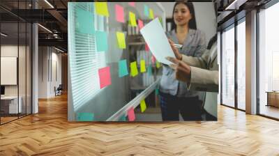 Two businesswomen are brainstorming and planning a project using a glass wall with sticky notes in an office Wall mural