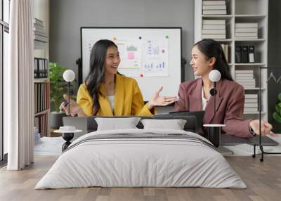 Two businesswomen are having a productive meeting, discussing business reports and analyzing financial data in their office Wall mural