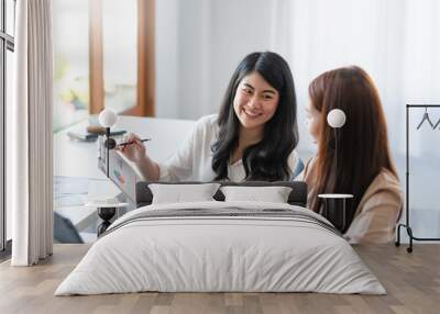 two pretty young asian businesswoman sitting at desk with laptop doing paperwork together discussing Wall mural