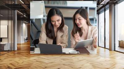 Two young beautiful asian business woman in the conversation, exchanging ideas at work. Wall mural