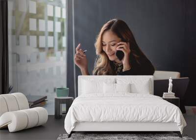 Young asian businesswoman beautiful charming smiling and talking on the mobile phone in the office. Wall mural