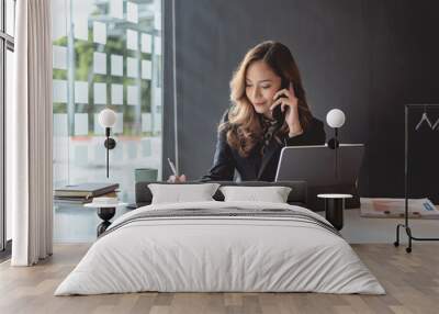 Young asian businesswoman beautiful charming smiling and talking on the mobile phone in the office. Wall mural