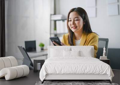 Young asian businesswoman happily using her smartphone in a modern office filled with productivity Wall mural