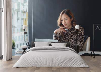 Young asian businesswoman sitting on her workplace in the office. Young woman working at laptop in the office. Wall mural