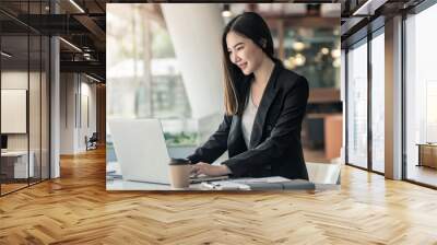 Young Asian businesswoman working on a laptop at a modern office. Wall mural