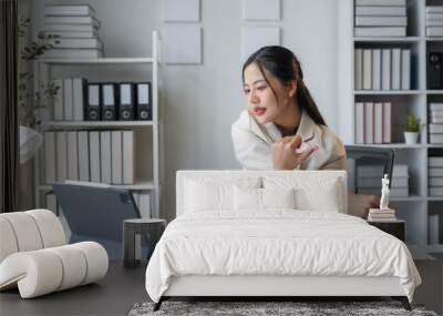 Young asian woman stretches while working on a laptop in her home office, balancing business tasks with health Wall mural