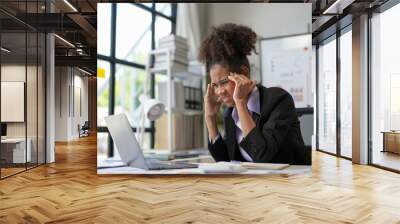 Young businesswoman having headache while working on laptop in office Wall mural