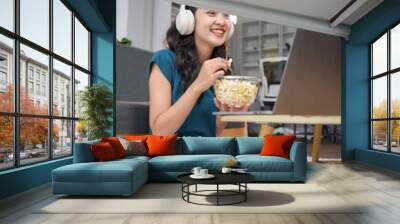 Young woman watching movie on laptop and eating popcorn at home Wall mural