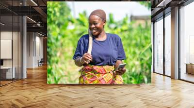 excited image of young african lady in a farm holding smart phone- black lady in maize farm Wall mural