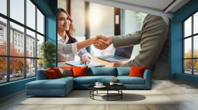 A young professional shaking hands with a new employer in an office setting. Wall mural