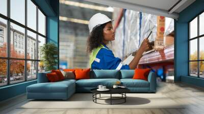 African American female warehouse worker wearing hard hat and uniform checks stock and inventory in warehouse. Woman worker working in storage warehouse. Black female worker working in storehouse Wall mural