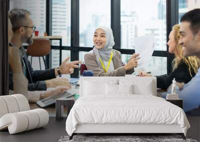 Asian Muslim business woman in hijab headscarf sitting on wheelchair presenting of her work to corporate colleagues in meeting in the modern office. diverse corporate colleagues and multicultural Wall mural