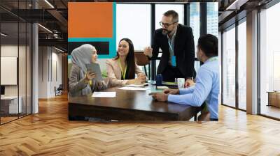 Asian Muslim business woman in hijab headscarf sitting on wheelchair presenting of her work to corporate colleagues in meeting in the modern office. diverse corporate colleagues and multicultural Wall mural