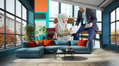 Asian Muslim businesswoman sitting on wheelchair presenting business graph on paper to manager. Smiling group of diverse corporate colleagues in the modern office. Diversity or multicultural in office Wall mural