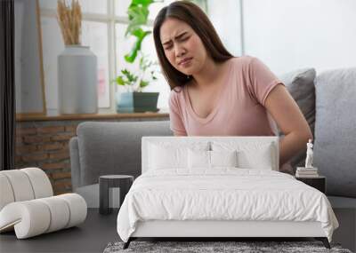 Asian woman have a stomach pain on the sofa at home. Wall mural