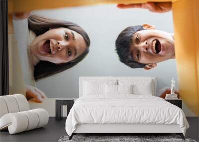 Cheerful Asian young couple opening cardboard box or parcel and looking inside Wall mural