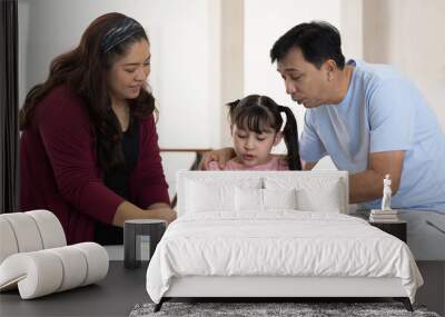 Diverse asian family with child daughter reading a book together at home. Smiling parents and teen daughter spending time together. Wall mural