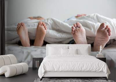 Elderly couple's feet sticking out from under the blanket during sleeping on bed together in bedroom at home Wall mural